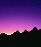 Photo of black mountain peaks in silhouette against a pink and indigo sunrise.